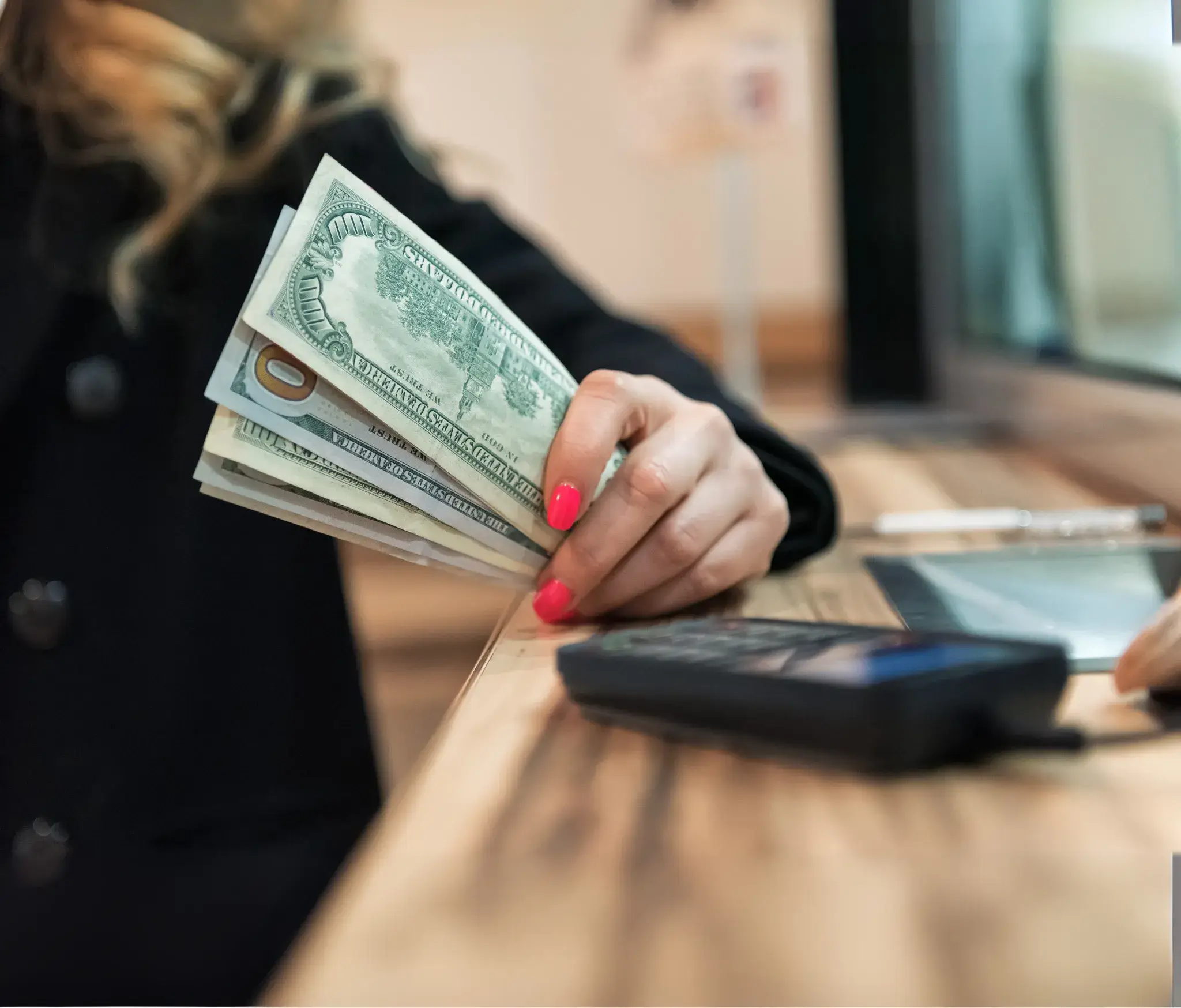 Person holding a fan of US dollar bills with a phone nearby on a wooden surface.