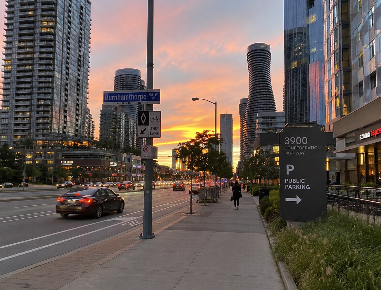A street view of city buildings, a busy intersection, and trees under a sunset sky.